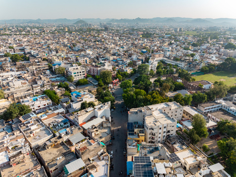 Aerial view of the dense urban landscape of Udaipur featuring traditional and modern buildings rooftops with solar panels and lush green trees in Udaipur Rajasthan India.
