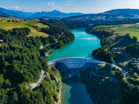 Aerial view of Barrage de Rossens spanning the turquoise waters of Lac de la Gruyere surrounded by lush green hills dense forests and meadows in Pont la Ville Fribourg Switzerland.