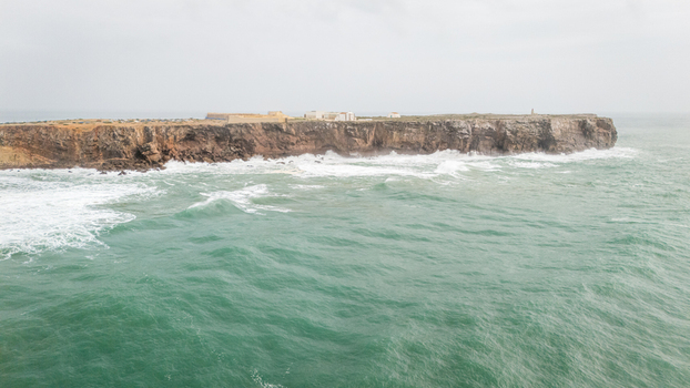 Aerial view of the Fortress of Sagres on a rocky promontory with waves crashing against the cliffs under an overcast sky in Sagres Faro Portugal. Aerial view of the Fortress of Sagres on a rocky promontory with waves crashing against the cliffs under an overcast sky in Sagres Faro Portugal.