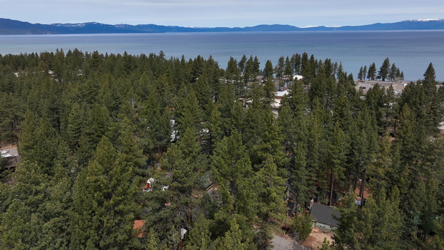 Aerial view of the dense pine forest surrounding the lake with blue waters and distant mountains in South Lake Tahoe California United States.