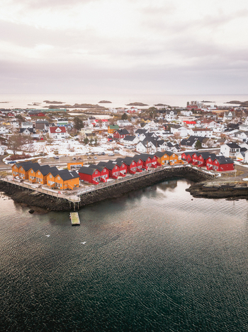 Aerial view of vibrant red and yellow buildings nestled against the calm dark water contrasting with the snow dusted landscape Ballstad Nordland Norway. Aerial view of vibrant red and yellow buildings nestled against the calm dark water contrasting with the snow dusted landscape Ballstad Nordland Norway.