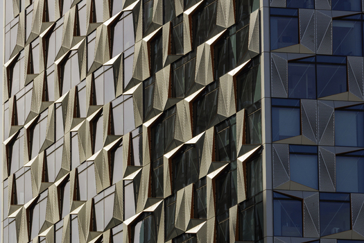 View of the geometric metal and glass facade of a modern skyscraper with angular panels reflecting light in London England United Kingdom.
