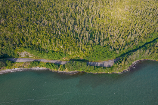 Aerial view of a coastal road winding through a dense evergreen forest along the shoreline in Juneau Alaska United States. Aerial view of a coastal road winding through a dense evergreen forest along the shoreline in Juneau Alaska United States.