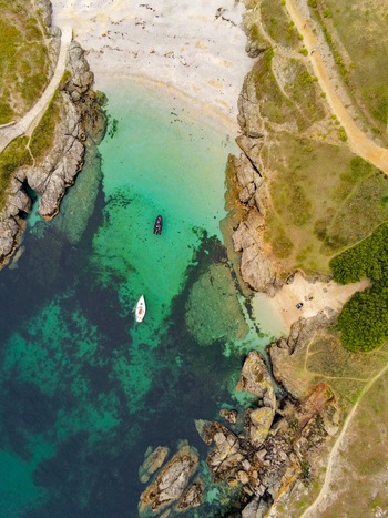 Aerial view of Pointe des Poulains featuring a turquoise cove with rocky cliffs sandy beach and small boats anchored in the clear water in Sauzon Bretagne France. Aerial view of Pointe des Poulains featuring a turquoise cove with rocky cliffs sandy beach and small boats anchored in the clear water in Sauzon Bretagne France.