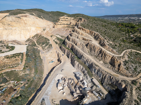 Aerial view of an active stone quarry with terraced rock faces heavy machinery and processing equipment in Teulada Valencian Community Spain.