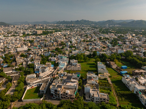 Aerial view of the dense urban landscape of Udaipur featuring residential rooftops green patches and distant hills under a clear sky in Udaipur Rajasthan India.