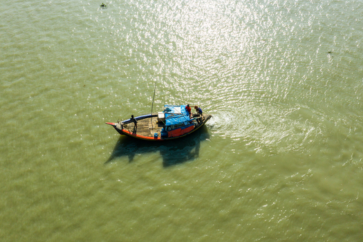 Aerial view of a wooden fishing boat with fishermen on board navigating the calm waters in Kuakata Barisal Division Bangladesh. Aerial view of a wooden fishing boat with fishermen on board navigating the calm waters in Kuakata Barisal Division Bangladesh.