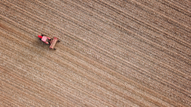 Aerial view of a red tractor ploughing a large textured field in Neuf Brisach Grand Est France. Aerial view of a red tractor ploughing a large textured field in Neuf Brisach Grand Est France.