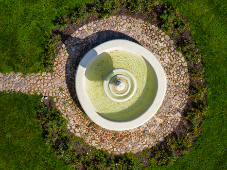 Aerial view of a tiered stone fountain with clear water surrounded by a circular cobblestone path and green lawn at Taujenai Manor park in Taujenai Vilnius County Lithuania.