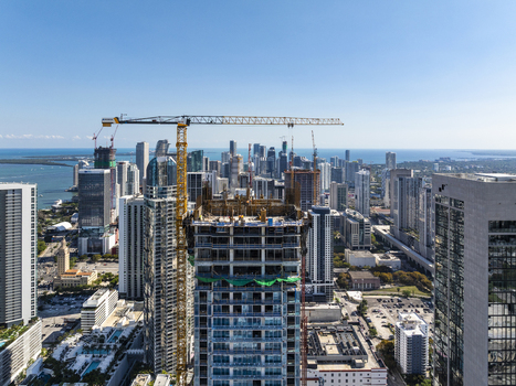 Aerial view of a skyscraper under construction piercing the skyline with cranes looming over the cityscape against the backdrop of Biscayne Bay Miami Florida USA. Aerial view of a skyscraper under construction piercing the skyline with cranes looming over the cityscape against the backdrop of Biscayne Bay Miami Florida USA.