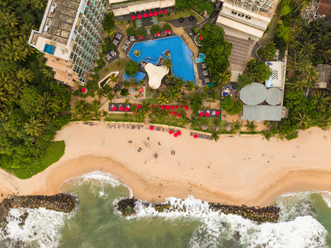 Aerial view of a luxury resort featuring a blue swimming pool and red umbrellas next to a sandy beach with ocean waves in Galle Southern Province Sri Lanka. Aerial view of a luxury resort featuring a blue swimming pool and red umbrellas next to a sandy beach with ocean waves in Galle Southern Province Sri Lanka.