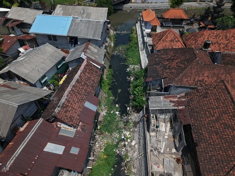Aerial view of a narrow canal flowing between dense residential buildings with red tiled roofs in Kecamatan Denpasar Barat Bali Indonesia. Aerial view of a narrow canal flowing between dense residential buildings with red tiled roofs in Kecamatan Denpasar Barat Bali Indonesia.