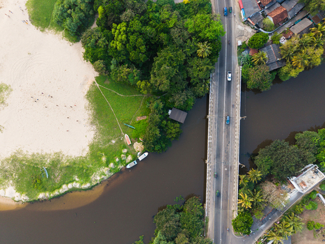 Aerial view of a bridge crossing a river next to a sandy beach and lush tropical forest with vehicles on the road in Galle Southern Province Sri Lanka.