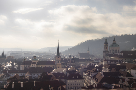 View of historic red rooftops and church spires under a hazy morning sky with Petrin Hill in the background in Prague Prague Czechia. View of historic red rooftops and church spires under a hazy morning sky with Petrin Hill in the background in Prague Prague Czechia.