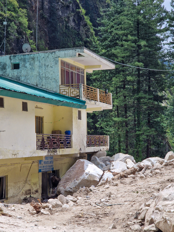View of a building damaged by large boulders from a landslide surrounded by pine trees and rocky terrain in Malana Himachal Pradesh India.