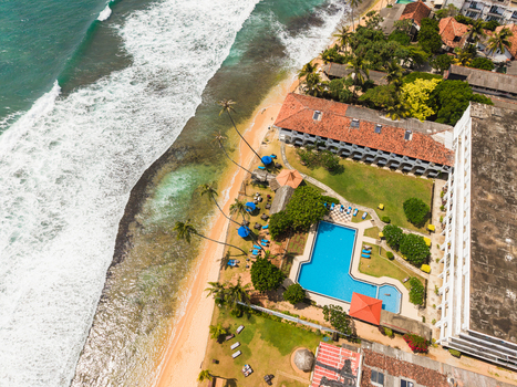 Aerial view of a beachfront resort with a swimming pool palm trees and turquoise ocean waves in Hikkaduwa Southern Province Sri Lanka. Aerial view of a beachfront resort with a swimming pool palm trees and turquoise ocean waves in Hikkaduwa Southern Province Sri Lanka.
