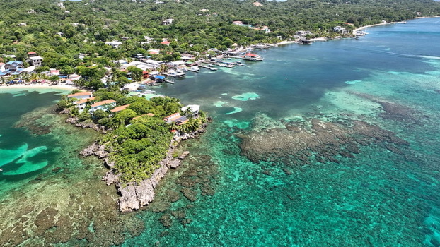 Aerial view of the coastal village with lush tropical vegetation turquoise coral reef waters and boats docked along the shore in West End Bay Islands Department Honduras. Aerial view of the coastal village with lush tropical vegetation turquoise coral reef waters and boats docked along the shore in West End Bay Islands Department Honduras.