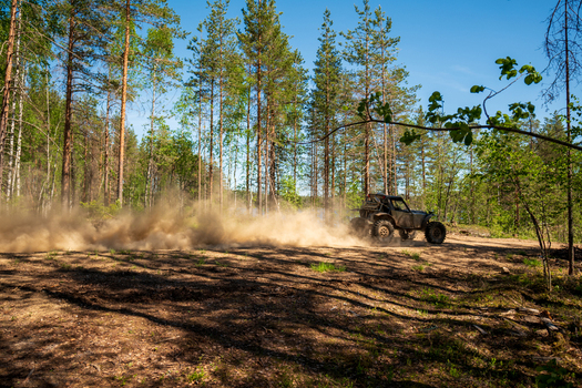 View of an off road buggy driving through a forest path near Lake Ladoga kicking up a cloud of dust in Sortavala Respublika Kareliya Russia.