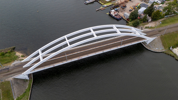 Aerial view of a modern white railway arch bridge spanning over a river with nearby industrial buildings and tracks in Gdansk Poland. Aerial view of a modern white railway arch bridge spanning over a river with nearby industrial buildings and tracks in Gdansk Poland.