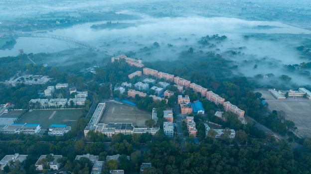 Aerial view of the town of Nagda surrounded by lush trees and a river shrouded in thick morning mist with residential buildings in Nagda Madhya Pradesh India. Aerial view of the town of Nagda surrounded by lush trees and a river shrouded in thick morning mist with residential buildings in Nagda Madhya Pradesh India.