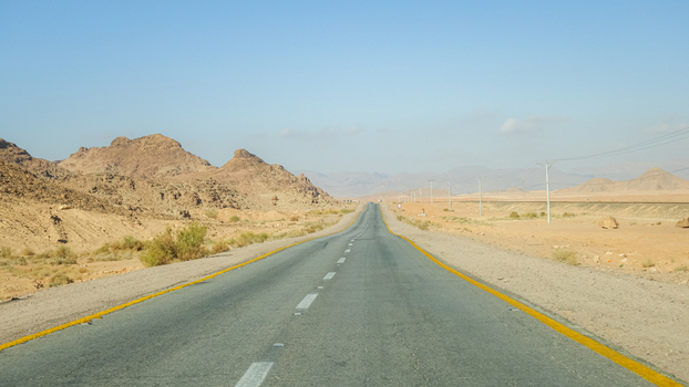 View of the asphalt road stretching through the Wadi Rum Desert landscape with rocky mountains under a clear sky in Wadi Rum Village Aqaba Governorate Jordan. View of the asphalt road stretching through the Wadi Rum Desert landscape with rocky mountains under a clear sky in Wadi Rum Village Aqaba Governorate Jordan.