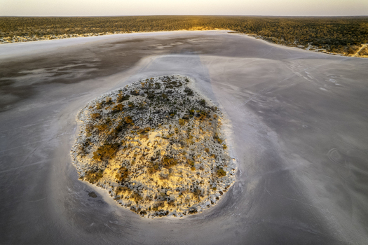 Aerial view of the salt pan at Googs Lake featuring a small vegetated island surrounded by arid wilderness in Yumbarra South Australia Australia.