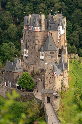 View of Eltz Castle with medieval stone towers and half timbered walls surrounded by lush green forest and people on the bridge in Wierschem Rhineland Palatinate Germany. View of Eltz Castle with medieval stone towers and half timbered walls surrounded by lush green forest and people on the bridge in Wierschem Rhineland Palatinate Germany.