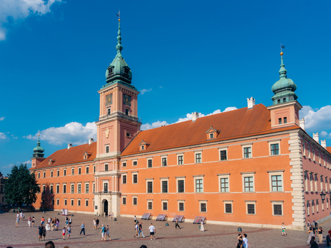 View of the historic Royal Castle in Warsaw Old Town with its pink facade and clock tower set against a clear blue sky with people walking in the square Warsaw Masovian Voivodeship Poland. View of the historic Royal Castle in Warsaw Old Town with its pink facade and clock tower set against a clear blue sky with people walking in the square Warsaw Masovian Voivodeship Poland.