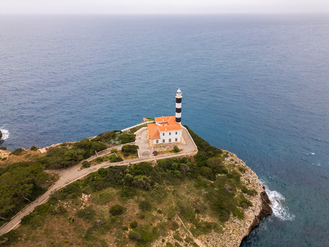 Aerial view of the Far de Portocolom lighthouse with its iconic black and white stripes on a rocky cliff overlooking the blue sea Portocolom Balearic Islands Spain. Aerial view of the Far de Portocolom lighthouse with its iconic black and white stripes on a rocky cliff overlooking the blue sea Portocolom Balearic Islands Spain.