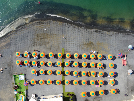 Aerial view of rows of orange and green sun umbrellas on a grey pebble beach by the turquoise sea in Imperia Liguria Italy. Aerial view of rows of orange and green sun umbrellas on a grey pebble beach by the turquoise sea in Imperia Liguria Italy.