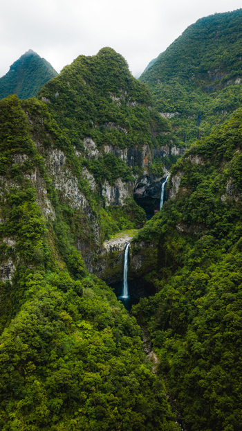 Aerial view of tall waterfalls cascading down lush green mountain slopes under a misty sky in La Reunion Nouvelle Aquitaine France. Aerial view of tall waterfalls cascading down lush green mountain slopes under a misty sky in La Reunion Nouvelle Aquitaine France.