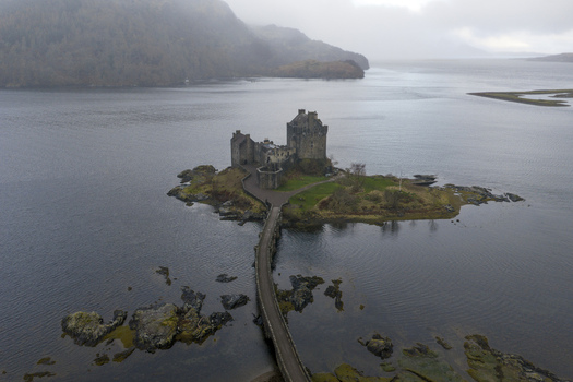 Aerial view of Eilean Donan Castle on a small island connected by a stone bridge over calm waters with misty hills in the background Dornie Scotland United Kingdom.