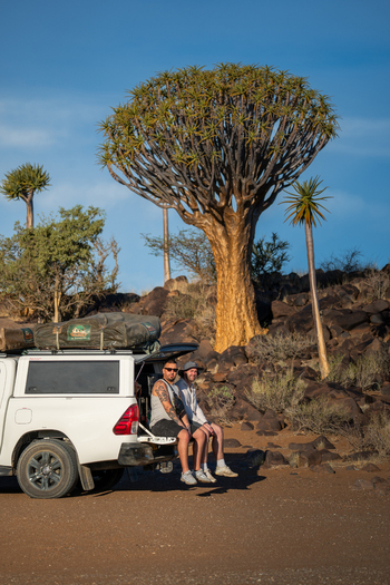 Aussenkehr Namibia 06 March 2026 View of two figures resting against a white vehicle juxtaposed against the distinctive silhouette of a quiver tree under a clear blue sky.. Aussenkehr Namibia 06 March 2026 View of two figures resting against a white vehicle juxtaposed against the distinctive silhouette of a quiver tree under a clear blue sky..