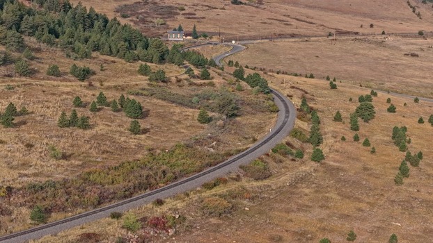 Aerial view of a winding railway track cutting through a dry grassy landscape with scattered pine trees and rolling hills in Golden Colorado United States.