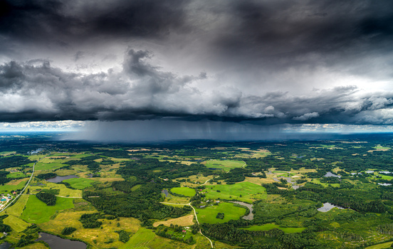 Aerial view of a dramatic storm front with heavy rain clouds over the green fields and forests of Latvia. Aerial view of a dramatic storm front with heavy rain clouds over the green fields and forests of Latvia.