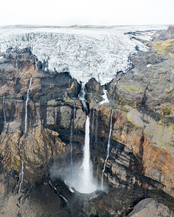 Aerial view of Langjokull glacier edge with cascading waterfalls flowing over dark volcanic rock cliffs in Vik Myrdalshreppur Iceland.