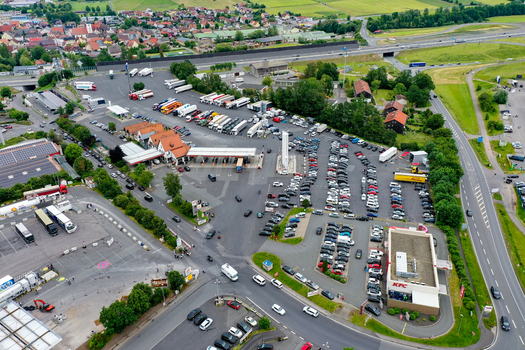 Geiselwind Germany 20 June 2025 Aerial view of a busy highway service area and truck stop with numerous parked trucks cars a gas station and commercial buildings.