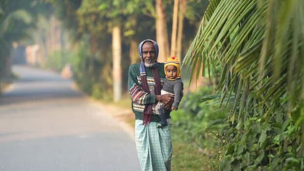 View of an elderly man holding a child on a rural road Bangladesh. View of an elderly man holding a child on a rural road Bangladesh.