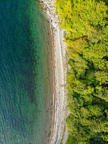 Aerial view of the rugged coastline featuring deep green waters a pebbly beach and dense forest canopy on the Isle of Skye Scotland United Kingdom. Aerial view of the rugged coastline featuring deep green waters a pebbly beach and dense forest canopy on the Isle of Skye Scotland United Kingdom.