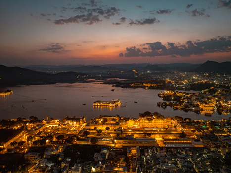 Aerial view of the illuminated City Palace and Lake Pichola in Udaipur at twilight with city lights reflecting on the water and surrounding hills in Udaipur Rajasthan India.