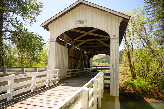 Aerial view of Stewart Bridge a historic wooden covered bridge spanning a river surrounded by lush green trees and foliage under a clear blue sky Washington USA. Aerial view of Stewart Bridge a historic wooden covered bridge spanning a river surrounded by lush green trees and foliage under a clear blue sky Washington USA.