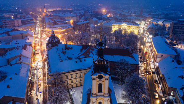 Aerial view of Saint Demetrius Cathedral surrounded by snow covered rooftops and illuminated streets in the historic city center of Sremska Mitrovica Vojvodina Serbia.