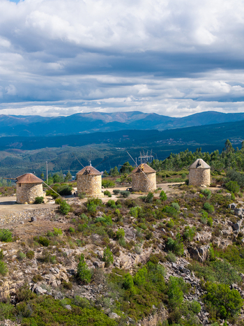 Aerial view of Moinhos da Serra da Atalhada featuring traditional stone windmills on a rocky ridge surrounded by green hills and a cloudy sky in Penacova Coimbra Portugal.