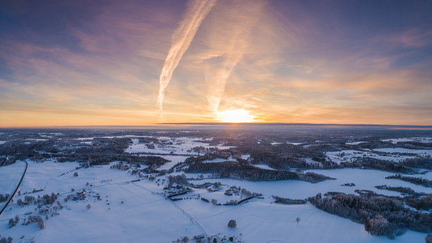 Aerial view of a vast snowy landscape during a golden sunset with contrails stretching across the sky Latvia. Aerial view of a vast snowy landscape during a golden sunset with contrails stretching across the sky Latvia.