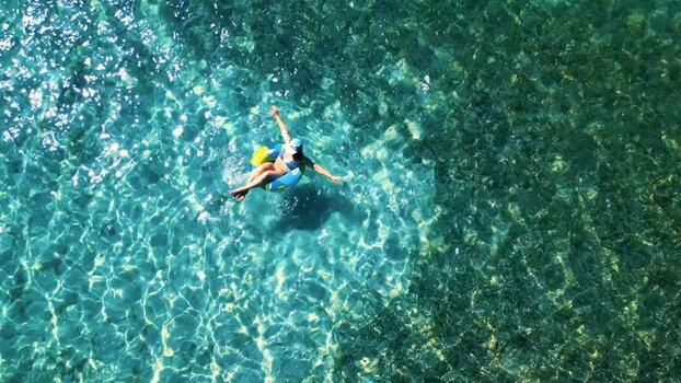 Aerial view of a woman floating in clear turquoise water Honduras.