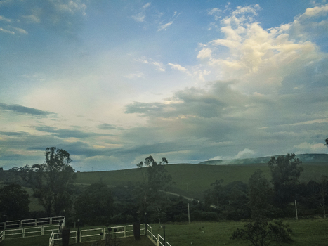Aerial view of a serene undulating green landscape under a dramatic sky with contrasting white and grey clouds Obudu Cross River Nigeria.