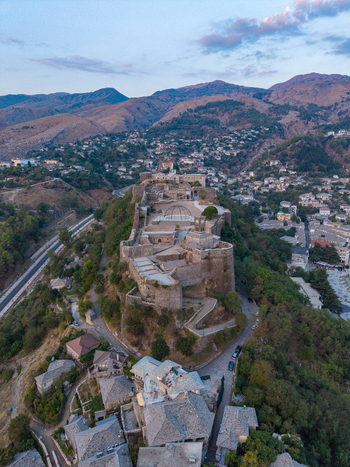 Aerial view of Gjirokaster Fortress with its historic stone walls and clock tower overlooking the traditional stone houses and mountains in Gjirokaster Gjirokaster County Albania. Aerial view of Gjirokaster Fortress with its historic stone walls and clock tower overlooking the traditional stone houses and mountains in Gjirokaster Gjirokaster County Albania.