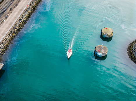 Aerial view of a small boat navigating through the turquoise waters of Bangor Harbour with concrete piers and calm sea Bangor Northern Ireland United Kingdom.