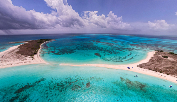 Aerial view of Los Roques archipelago featuring turquoise waters white sandbars and coral reefs under a dramatic cloudy sky in Los Roques Dependencias Federales Venezuela. Aerial view of Los Roques archipelago featuring turquoise waters white sandbars and coral reefs under a dramatic cloudy sky in Los Roques Dependencias Federales Venezuela.