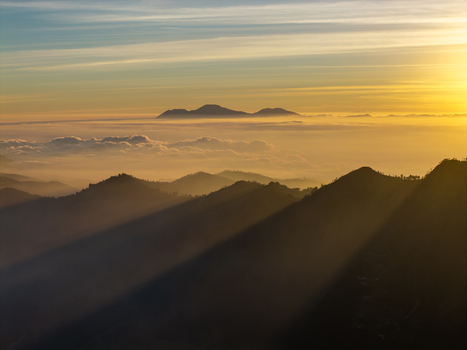 Aerial view of Cemorolawang during sunset with dramatic light rays illuminating the mountain peaks rolling hills and a sea of clouds in Kecamatan Sukapura Jawa Timur Indonesia.